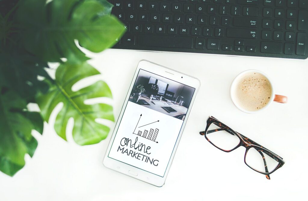 Tablet on desk showing online marketing growth chart, alongside coffee, glasses, and keyboard — symbolizing KeyBuzz Digital’s balanced approach to smart, data-driven marketing for small businesses.