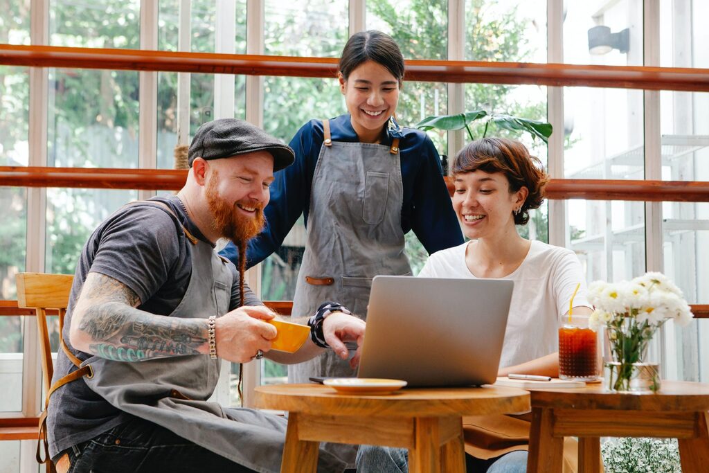 Small business owners in aprons smiling and collaborating on marketing strategy with a laptop in a cozy café setting   keybuzz digital marketing services