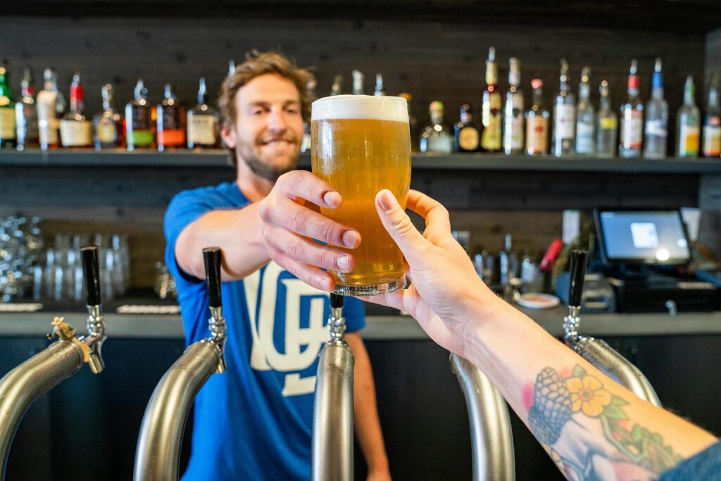 Bartender serving a fresh pint of beer across the bar, symbolizing hospitality service, customer experience, and local business marketing